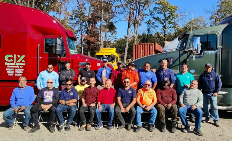 A group photo of drivers sitting in front of two trucks facing eachother.